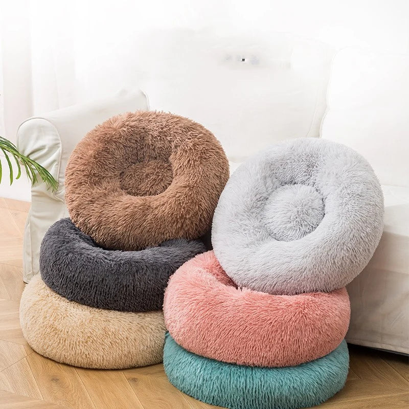 All Dogs Love plush round calming pet beds in various colors stacked together on a wooden floor.